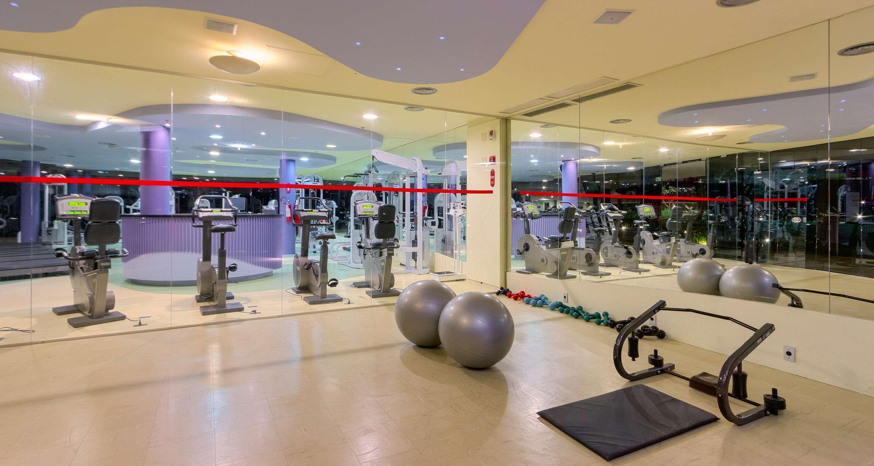 로열 튤립 브라질리아 알보라다 호텔 외부 사진 The photo depicts a gym or fitness area. In the foreground, there are two large exercise balls and a mat on the floor. Behind them, there is a wall of mirrors that reflects various gym equipment, including exercise machines and bikes. The lighting in