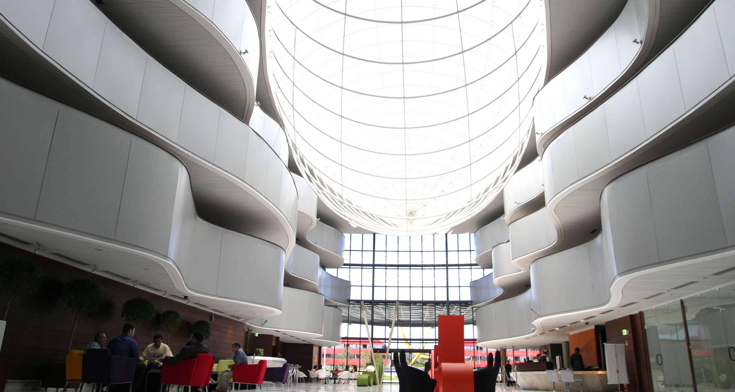 로열 튤립 브라질리아 알보라다 호텔 외부 사진 The photo depicts a modern interior space characterized by sleek, curvilinear architecture. The ceiling features a large, dome-like skylight that allows natural light to flood the area. The walls display a minimalist design with smooth, white surface