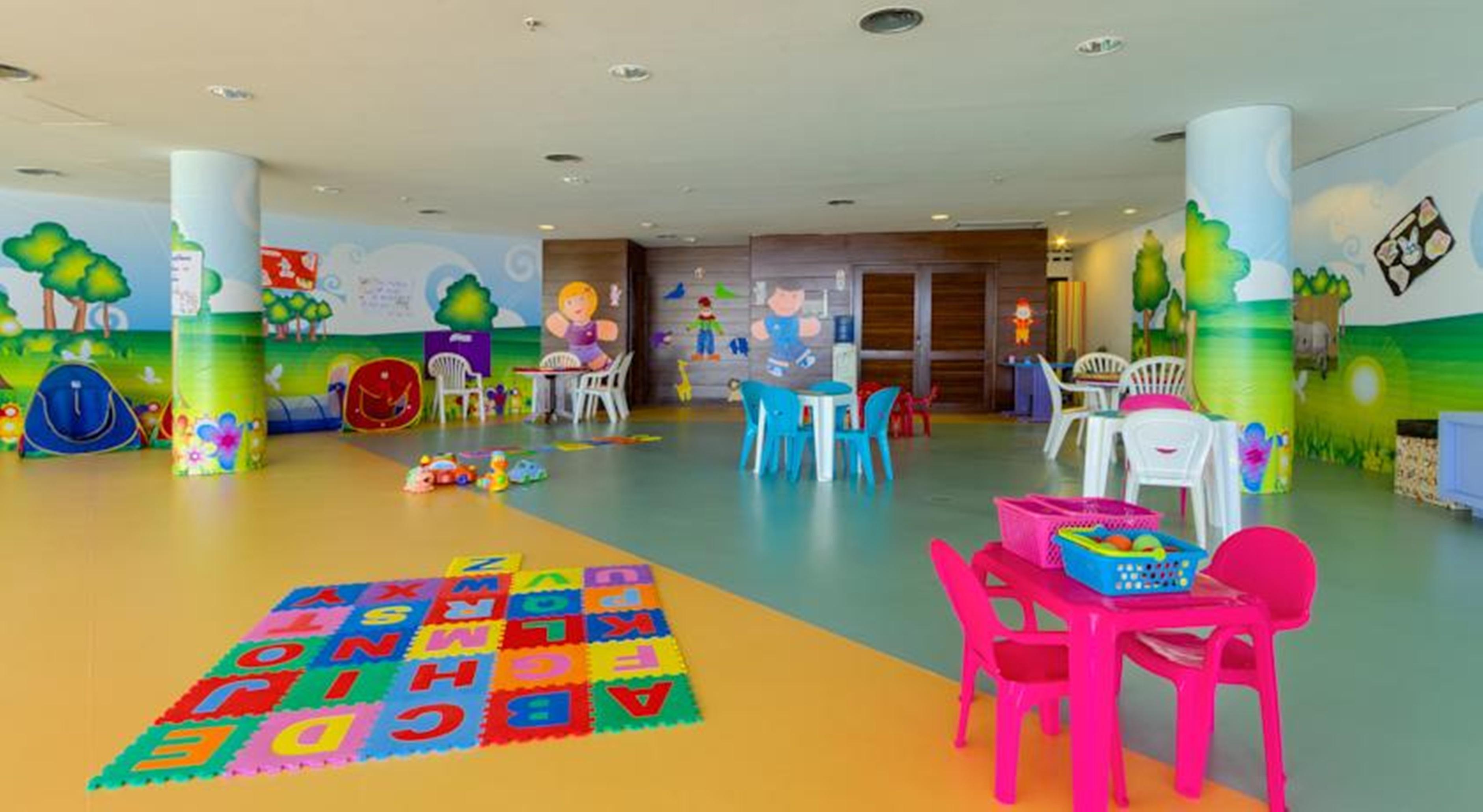 로열 튤립 브라질리아 알보라다 호텔 외부 사진 The photo shows a colorful and spacious children's playroom. The floor is divided into sections with different colors, and there is a large play mat featuring letters and numbers. 

In the room, there are several small, lightweight tables and chairs 